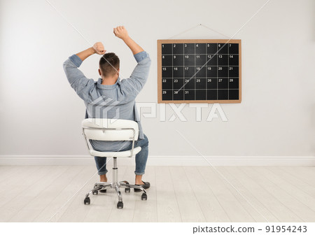 Young man sitting near board calendar indoors, back view Young man sitting near board calendar indoors, back view 91954243