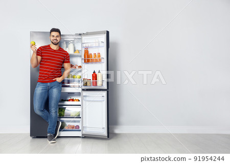 Happy young man with apple near open refrigerator indoors, space for text Happy young man with apple near open refrigerator indoors, space for text 91954244