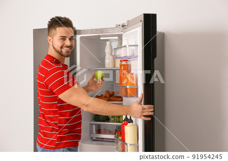 Young man taking fresh apple out of refrigerator Young man taking fresh apple out of refrigerator 91954245