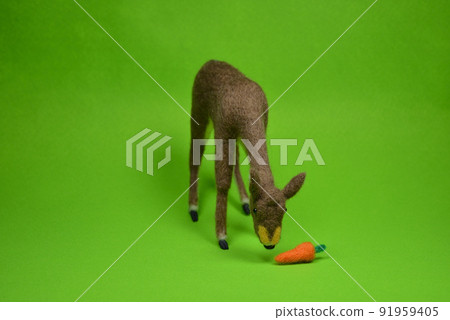 Felt doll with a deer eating carrots on a green background Felt doll with a deer eating carrots on a green background 91959405