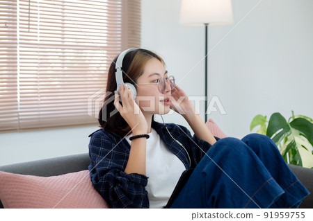 Happy Asian glasses girl listening music from headphone in living room at home. Recreation at home concept. Happy Asian glasses girl listening music from headphone in living room at home. Recreation at home concept. 91959755
