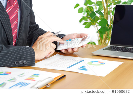A man doing calculations with a calculator on his desk 91960622