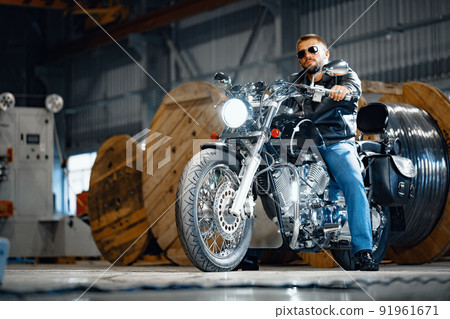 Bearded motorcyclist in black leather clothing with his motorbike Bearded motorcyclist in black leather clothing with his motorbike 91961671