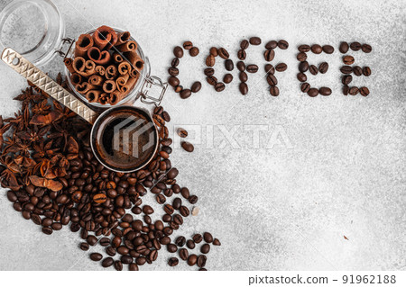 Word coffee made of roasted beans with copper turk and cinnamon sticks on light coloured surface 91962188
