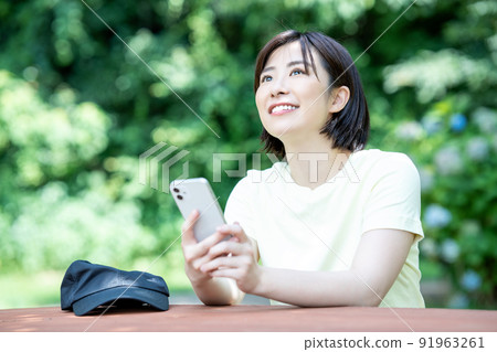 A woman using a smartphone at a table in a fresh green park 91963261