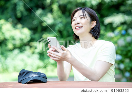 A woman using a smartphone at a table in a fresh green park 91963263