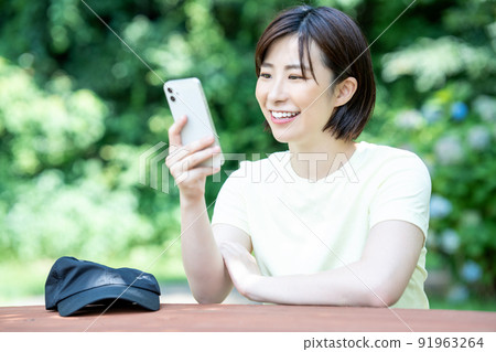 A woman using a smartphone at a table in a fresh green park A woman using a smartphone at a table in a fresh green park 91963264