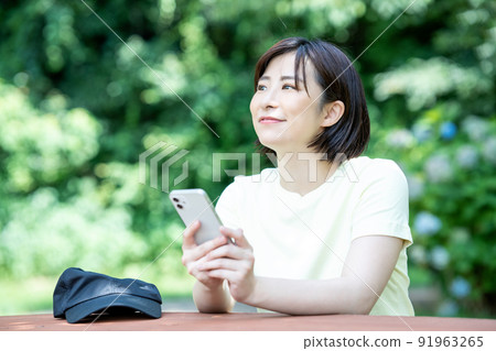 A woman using a smartphone at a table in a fresh green park A woman using a smartphone at a table in a fresh green park 91963265