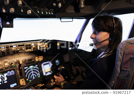 Aircrew member flying plane from cockpit with dashboard command and control panel, using steering wheel and control panel for windscreen navigation. Woman using lever to fly aircraft. Aircrew member flying plane from cockpit with dashboard command and control panel, using steering wheel and control panel for windscreen navigation. Woman using lever to fly aircraft. 91967217