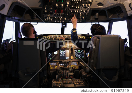 Captain and woman copilot getting ready to fly airplane and takeoff with dashboard navigation in cockpit command. Airline crew fixing altitude level and with control panel buttons, flying plane. 91967249