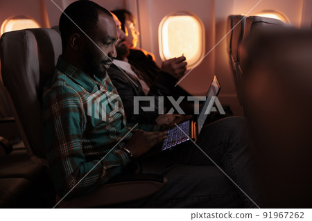 Modern traveller browsing internet on laptop and flying abroad in airplane, using international airline to travel on business work trip. Young man working on computer and travelling during sunset. Modern traveller browsing internet on laptop and flying abroad in airplane, using international airline to travel on business work trip. Young man working on computer and travelling during sunset. 91967262