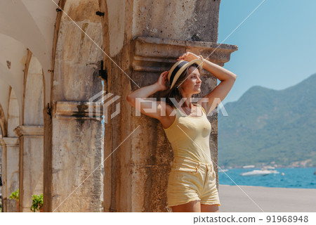 Summer photo shoot on the streets of Kotor, Montenegro. Beautiful girl in yellow dress and hat. smiling tourist girl with hat. Spectacular view of Montenegro with copy space. fashion outdoor photo of 91968948