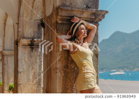 Summer photo shoot on the streets of Kotor, Montenegro. Beautiful girl in white dress and hat. smiling tourist girl with hat. Spectacular view of Montenegro with copy space. fashion outdoor photo of 91968949