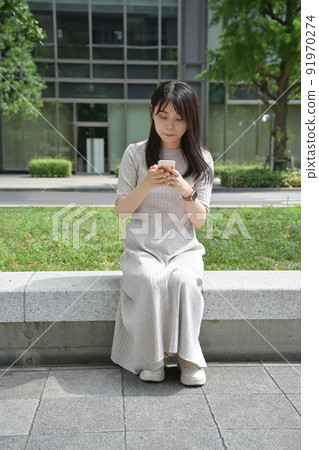 A young woman sitting on a bench and looking at her smartphone 91970274