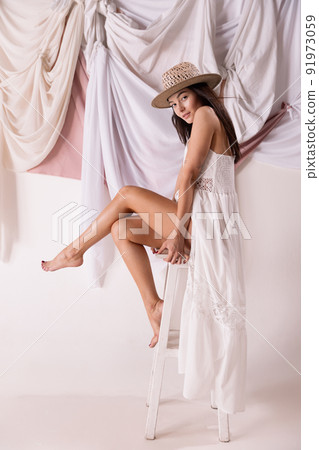 Portrait of stylish woman sitting on chair, posing in white dress and straw hat isolated over textile background 91973059