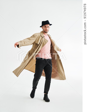 Happy smiling man in beige trench coat spinning around over white background 91974978