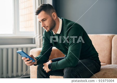 Relaxed man sitting on couch using hsi mobile smart phone 91975004
