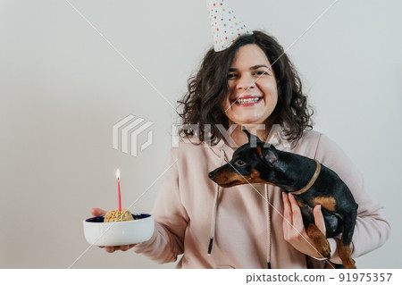 Happy young girl giving homemade cake to her dog, indoors 91975357