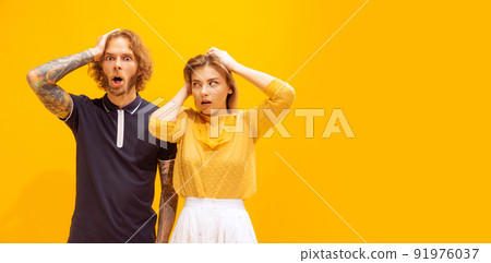 Portrait of young man and woman in casual clothes posing isolated over yellow studio background. Showing shocked expression. Flyer Portrait of young man and woman in casual clothes posing isolated over yellow studio background. Showing shocked expression. Flyer 91976037