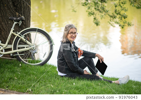 A woman with a tablet sitting near the river and resting 91976043