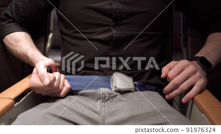 Unrecognizable businessman passenger onboard fastening a seat belt while sitting in the airplane. Safety regulation and instruction in commercial airline flight concept. 91976324