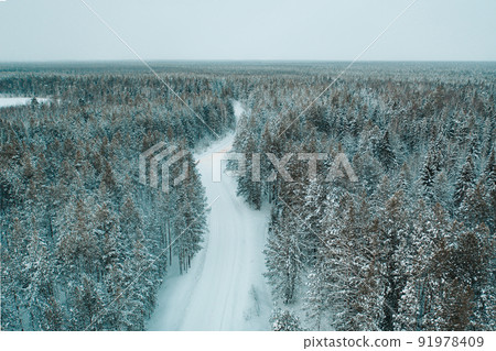 Aerial drone view of snowy winter road in forest with light lines from car 91978409