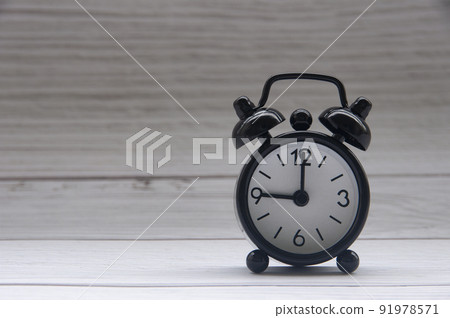 Black alarm clock isolated on white wooden cover background. The clock set at 9 o'clock. Copy space. Black alarm clock isolated on white wooden cover background. The clock set at 9 o'clock. Copy space. 91978571