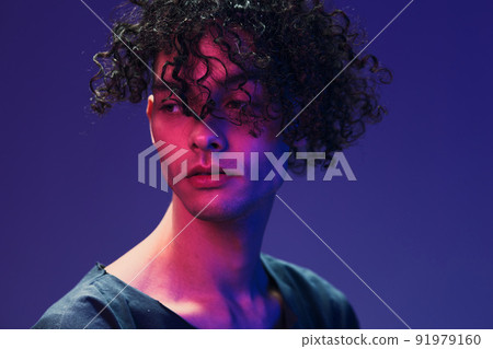 Fashionable handsome curly man in black t-shirt looks aside posing isolated on color pink blue studio background. Cool fashion offer. Virtual Reality New Collection concept. Copy space for ad Fashionable handsome curly man in black t-shirt looks aside posing isolated on color pink blue studio background. Cool fashion offer. Virtual Reality New Collection concept. Copy space for ad 91979160