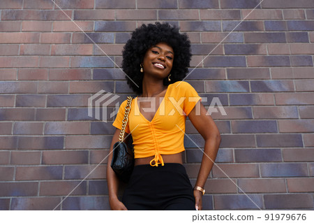 Portrait of young black woman with afro hairstyle smiling in urban background 91979676