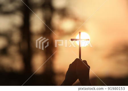 黃色的夕陽天空和明亮的陽光背景以及手中十字架的輪廓 91980153