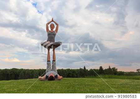 Young couple doing acro yoga in park. Man lying on grass and balancing woman in his feet Young couple doing acro yoga in park. Man lying on grass and balancing woman in his feet 91980583