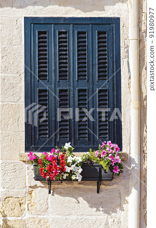 Closed wooden window shutter in window frame with potted flowers on windowsill 91980977