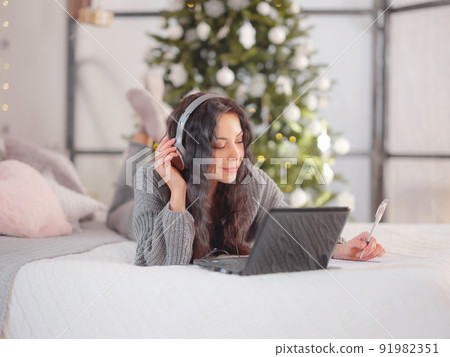 woman in cozy grey knitted sweater using laptop on bed , xmas holiday woman in cozy grey knitted sweater using laptop on bed , xmas holiday 91982351