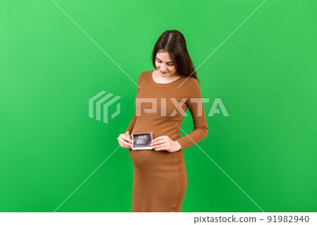 Cute Pregnant Lady Posing With Baby Sonography Photo Near Colored background. Concept of pregnancy, gynecology, medical test, maternal health 91982940