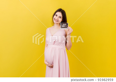 Cute Pregnant Lady Posing With Baby Sonography Photo Near Colored background. Concept of pregnancy, gynecology, medical test, maternal health 91982959