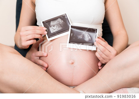 Portrait of young happy married couple hold ultrasound picture. Diverse man and pregnant woman show sonogram image on kid child, excited for parenthood. Parenting concept Portrait of young happy married couple hold ultrasound picture. Diverse man and pregnant woman show sonogram image on kid child, excited for parenthood. Parenting concept 91983016