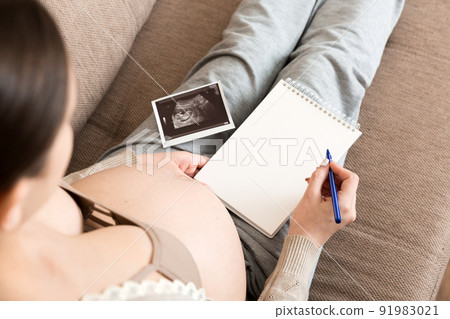Top view caring future mother writing diary with ultrasound. pregnant woman tummy making notes feeling during pregnancy or creating scrapbook Top view caring future mother writing diary with ultrasound. pregnant woman tummy making notes feeling during pregnancy or creating scrapbook 91983021
