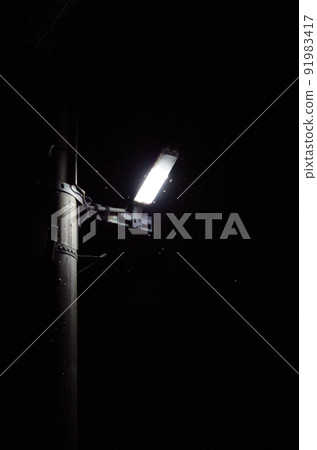 夏季夜間戶外場景的高靈敏度圖像,許多昆蟲在電線桿上安裝的燈周圍成群結隊。 夏季夜間戶外場景的高靈敏度圖像,許多昆蟲在電線桿上安裝的燈周圍成群結隊。 91983417