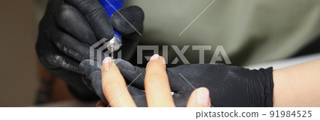 Nail master using electrical equipment to clean client nails in modern beauty studio 91984525