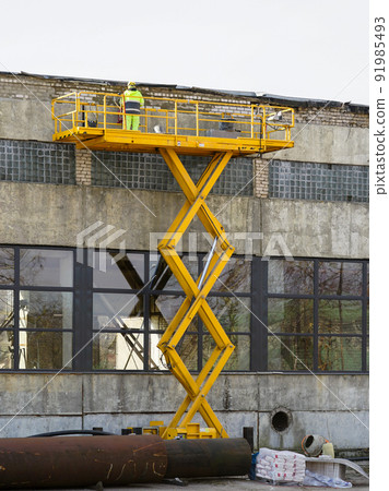 Yellow self propelled scissor lift in action with worker in uniform and safety protective equipment Yellow self propelled scissor lift in action with worker in uniform and safety protective equipment 91985493