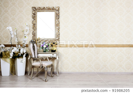 A fragment of a retro interior with a chair and table, on which is a telephone and a vase of flowers. Above the table hangs an empty picture frame for your photo 91986205