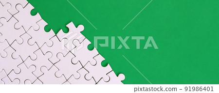 Fragment of a folded white jigsaw puzzle on the background of a green plastic surface. Texture photo with copy space for text Fragment of a folded white jigsaw puzzle on the background of a green plastic surface. Texture photo with copy space for text 91986401