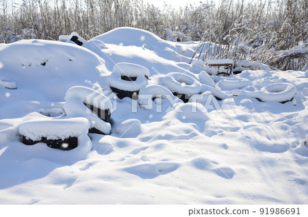 Used and discarded car tires lie on the side of the road, covered with a thick layer of snow 91986691