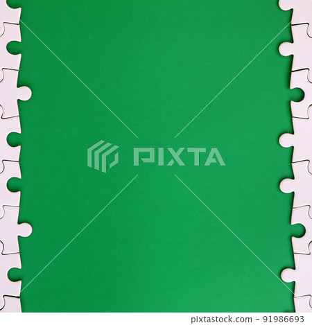 Fragment of a folded white jigsaw puzzle on the background of a green plastic surface. Texture photo with copy space for text 91986693