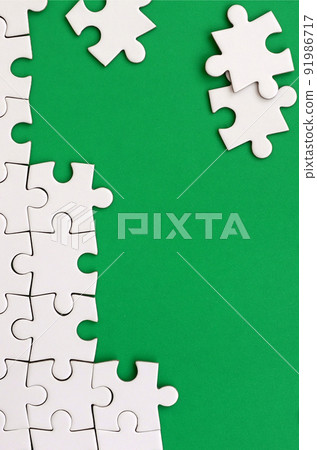 Fragment of a folded white jigsaw puzzle and a pile of uncombed puzzle elements against the background of a green surface. Texture photo with space for text Fragment of a folded white jigsaw puzzle and a pile of uncombed puzzle elements against the background of a green surface. Texture photo with space for text 91986717