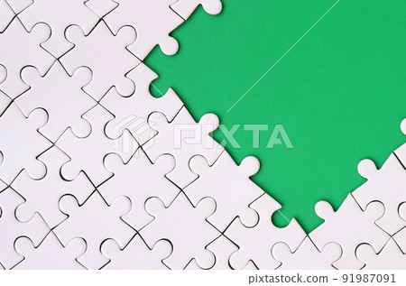 Fragment of a folded white jigsaw puzzle on the background of a green plastic surface. Texture photo with copy space for text 91987091