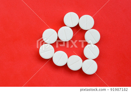 Several white tablets lie on a bright red background in the shape of a heart. Background image on medicine and pharmaceutical topics Several white tablets lie on a bright red background in the shape of a heart. Background image on medicine and pharmaceutical topics 91987182