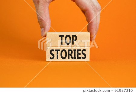 Top stories symbol. Concept words Top stories on wooden blocks on a beautiful orange table orange background. Businessman hand. Business story and top stories concept, copy space. Top stories symbol. Concept words Top stories on wooden blocks on a beautiful orange table orange background. Businessman hand. Business story and top stories concept, copy space. 91987310