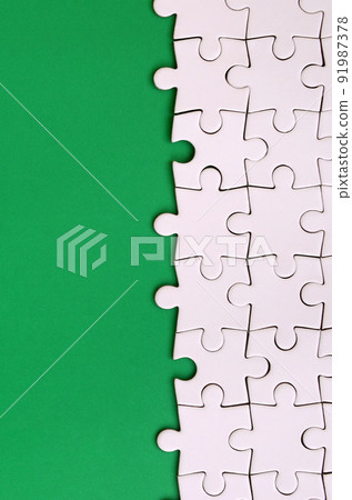Fragment of a folded white jigsaw puzzle on the background of a green plastic surface. Texture photo with copy space for text 91987378