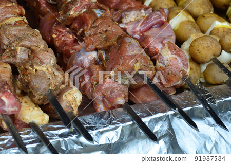 Raw meat and potatoes are planted on metal skewers. The process of cooking shish kebabs. Russian and Ukrainian camp food Raw meat and potatoes are planted on metal skewers. The process of cooking shish kebabs. Russian and Ukrainian camp food 91987584